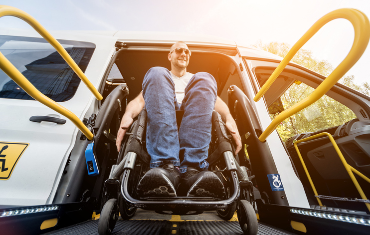 A man in a wheelchair on a lift of a vehicle for people with disabilities