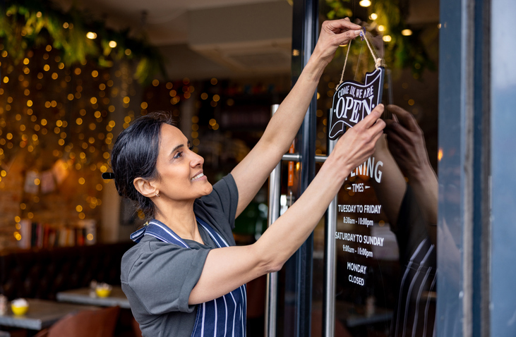 Business owner hanging an open sign on the door at a cafe